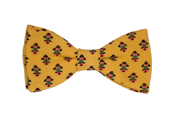 Nœud papillon en tissu provençal jaune orné de motifs calissons rouges, noirs et verts, un clin d'œil à la tradition provençale.